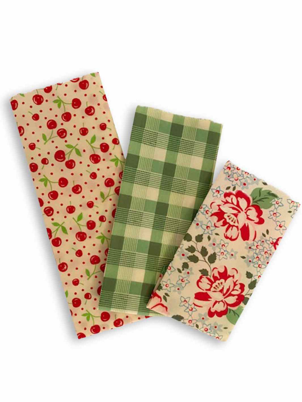 Good Soul Shop Set of three beeswax food wraps in red cherries, green plaid, and red floral pattern fanned out