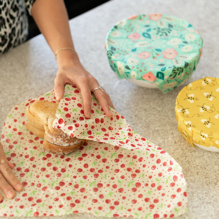 Caucasian woman folding bread in Good Soul Shop cherry beeswax wraps - two bowls with floral and bee beeswax wraps are off to the side