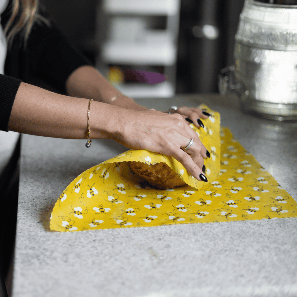 Woman wrapping loaf of bread with beeswax wrap in a yellow bee pattern